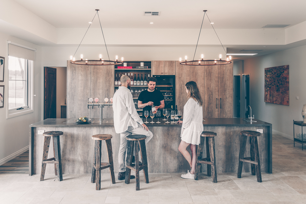 Man pouring wine at bar for a man and woman at wine tasting